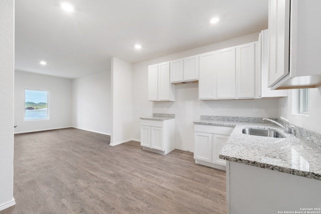 kitchen featuring white cabinets, sink, light wood-type flooring, and light stone counters