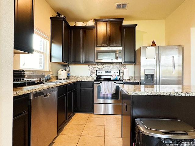 kitchen featuring light stone counters, dark brown cabinetry, light tile patterned flooring, sink, and stainless steel appliances