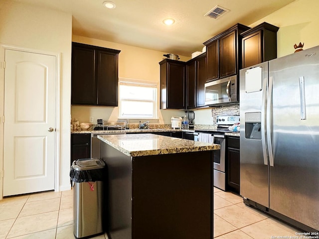 kitchen with light stone countertops, appliances with stainless steel finishes, light tile patterned floors, and a center island