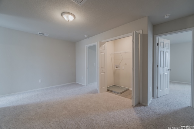 unfurnished bedroom featuring light carpet, a textured ceiling, a closet, and a spacious closet