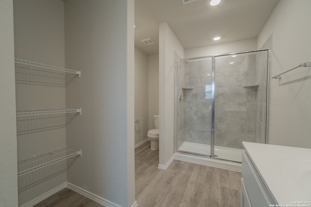 bathroom with hardwood / wood-style floors, a shower with shower door, vanity, and toilet