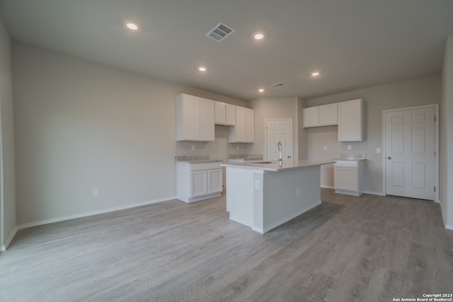 kitchen with white cabinets, sink, a center island with sink, and light hardwood / wood-style floors