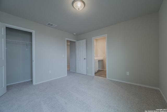 unfurnished bedroom with a closet, ensuite bathroom, and light carpet