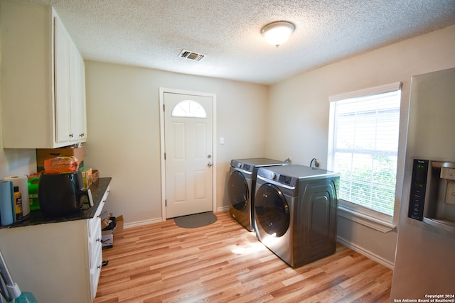 laundry area featuring washer and dryer, cabinets, light wood-type flooring, and a textured ceiling