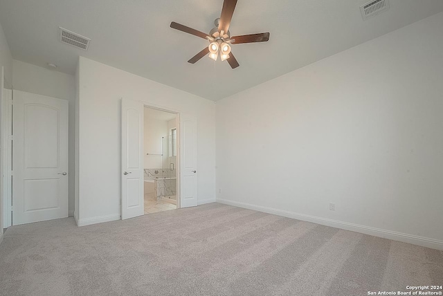 unfurnished bedroom featuring ensuite bathroom, light colored carpet, and ceiling fan