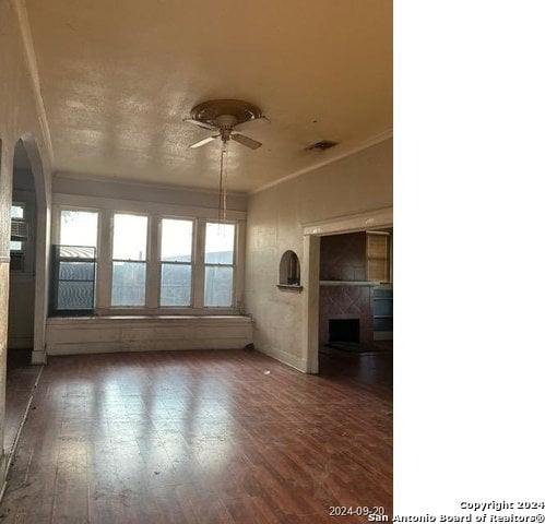 spare room featuring ceiling fan, dark hardwood / wood-style floors, ornamental molding, and a tiled fireplace