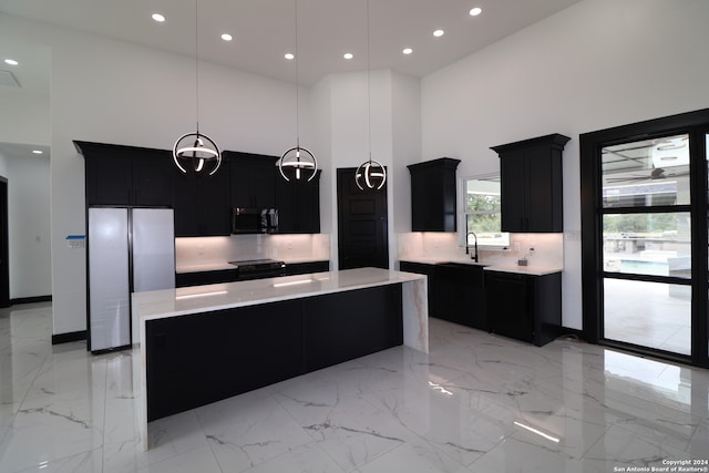 kitchen with a towering ceiling, hanging light fixtures, appliances with stainless steel finishes, and a kitchen island