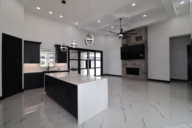 kitchen with beamed ceiling, pendant lighting, a kitchen island, a towering ceiling, and a fireplace