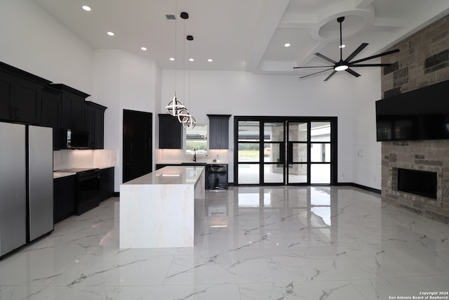 kitchen with a high ceiling, a kitchen island, stainless steel fridge, and hanging light fixtures