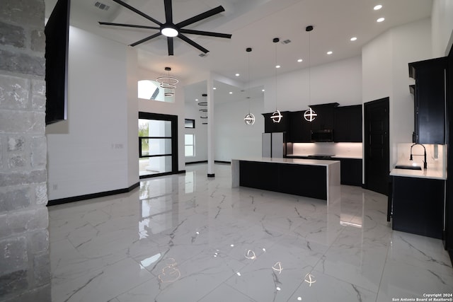 kitchen with ceiling fan, sink, decorative light fixtures, a center island, and a towering ceiling