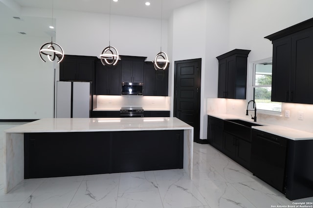 kitchen featuring a kitchen island, sink, a high ceiling, appliances with stainless steel finishes, and decorative light fixtures