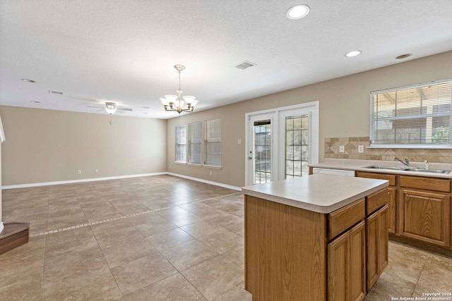 kitchen with sink, a textured ceiling, decorative light fixtures, a center island, and ceiling fan with notable chandelier