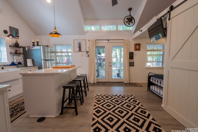 kitchen with light wood-type flooring, white cabinets, stainless steel refrigerator, a barn door, and decorative light fixtures