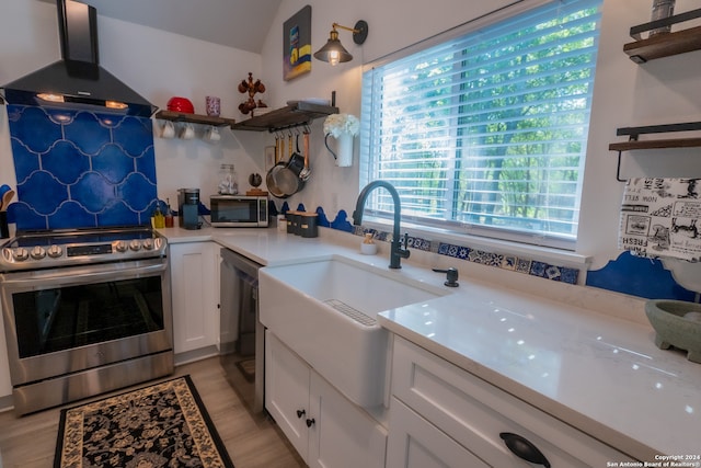 kitchen featuring sink, light hardwood / wood-style flooring, wall chimney exhaust hood, white cabinetry, and stainless steel appliances