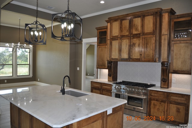 kitchen featuring light wood-type flooring, hanging light fixtures, sink, double oven range, and an island with sink