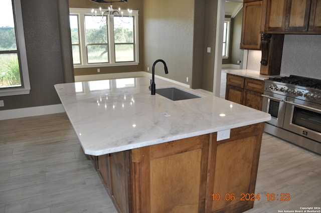 kitchen with light stone counters, a kitchen island with sink, sink, and double oven range