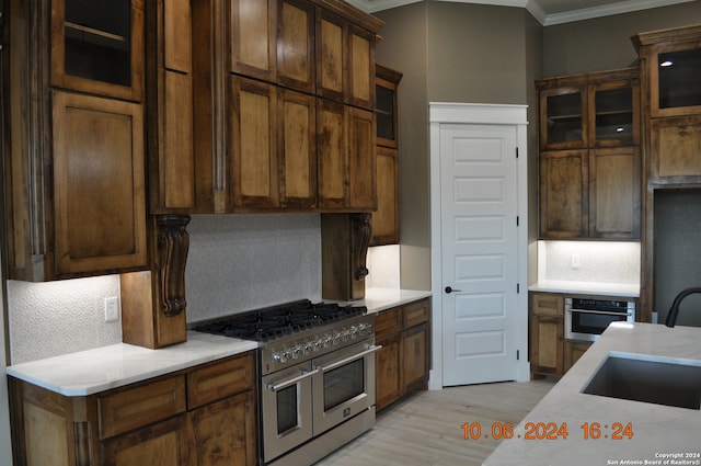 kitchen with appliances with stainless steel finishes, light wood-type flooring, ornamental molding, and tasteful backsplash