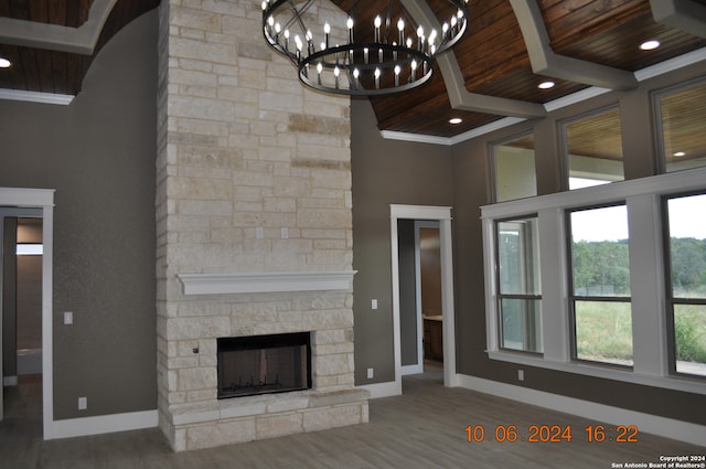 unfurnished living room featuring hardwood / wood-style floors, wood ceiling, a fireplace, a notable chandelier, and a towering ceiling