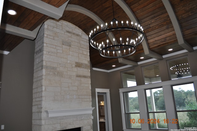 interior space featuring beamed ceiling, a stone fireplace, wood ceiling, and an inviting chandelier