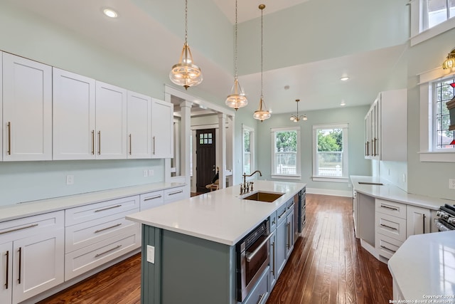 kitchen featuring dark wood-type flooring, an island with sink, sink, pendant lighting, and white cabinets