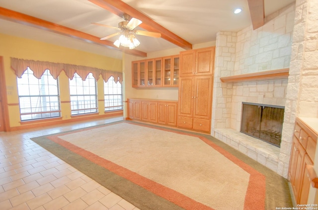 unfurnished living room with beam ceiling, ceiling fan, light tile patterned flooring, and a stone fireplace