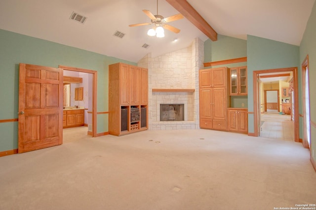 unfurnished living room with beam ceiling, light colored carpet, ceiling fan, and a stone fireplace