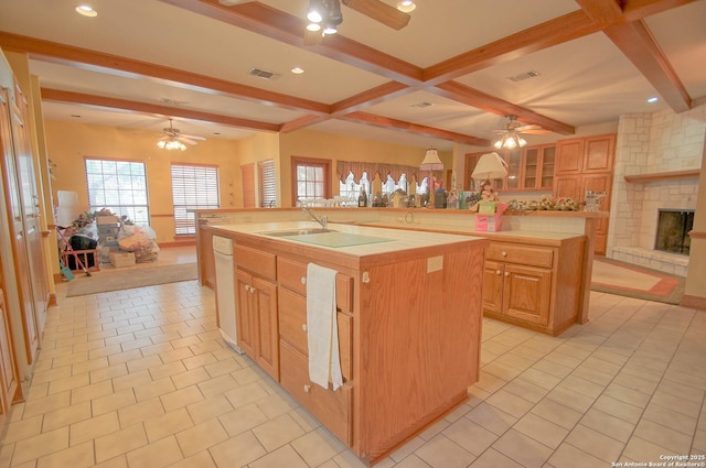 kitchen with beamed ceiling, a fireplace, an island with sink, white dishwasher, and light tile patterned floors