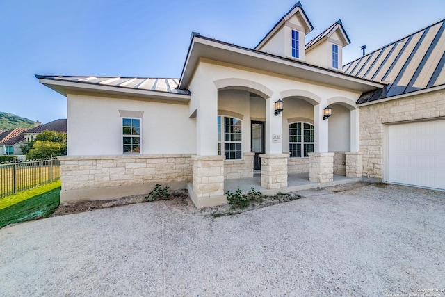 view of front facade featuring a standing seam roof, covered porch, metal roof, stone siding, and a garage