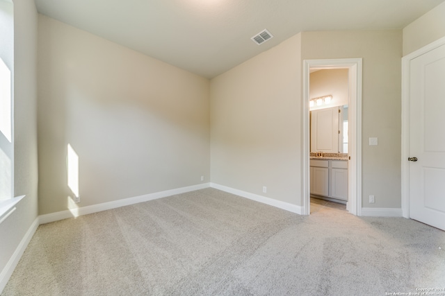 unfurnished bedroom with ensuite bathroom and light carpet