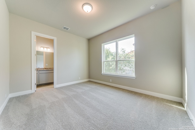 unfurnished bedroom featuring ensuite bathroom and light carpet