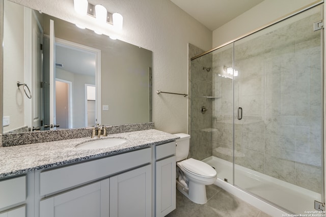 bathroom featuring tile patterned flooring, toilet, a shower with door, and vanity