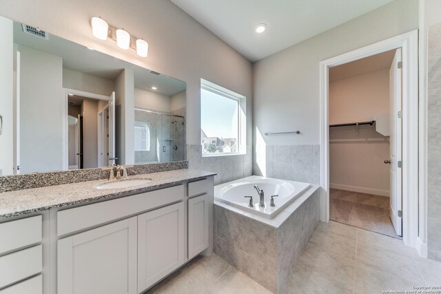bathroom with a garden tub, vanity, a walk in closet, a stall shower, and tile patterned floors