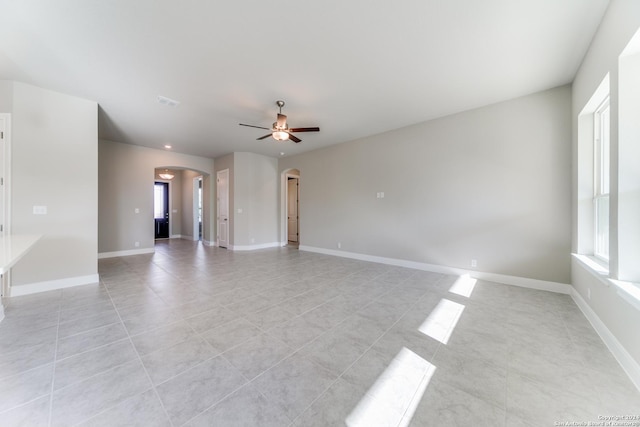 unfurnished living room with light tile patterned floors, ceiling fan, arched walkways, and a healthy amount of sunlight