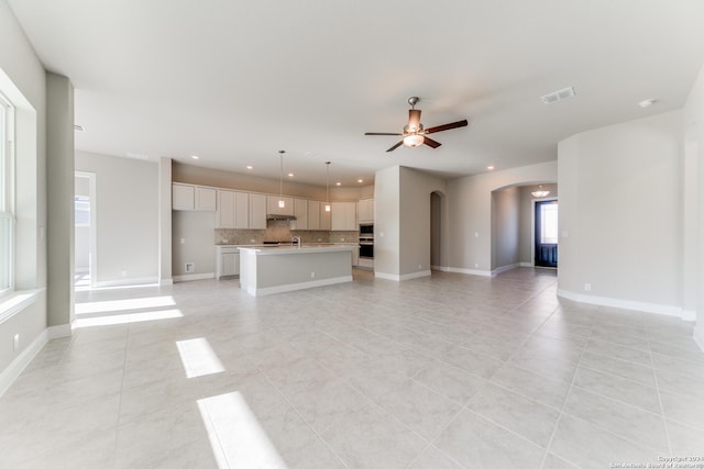 unfurnished living room featuring visible vents, a ceiling fan, arched walkways, and light tile patterned floors