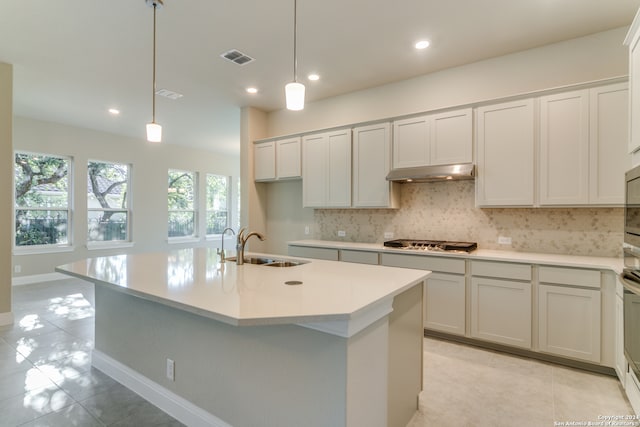 kitchen with tasteful backsplash, stainless steel gas stovetop, sink, hanging light fixtures, and an island with sink