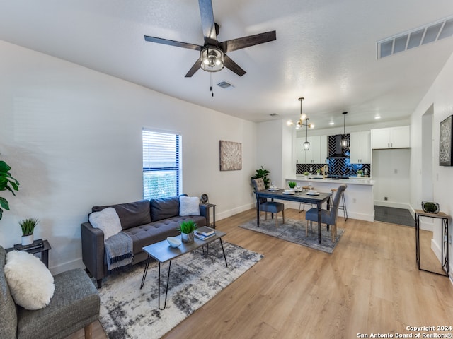 living room with ceiling fan with notable chandelier and light hardwood / wood-style flooring