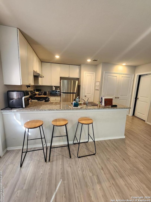 kitchen with kitchen peninsula, white cabinets, appliances with stainless steel finishes, and light wood-type flooring