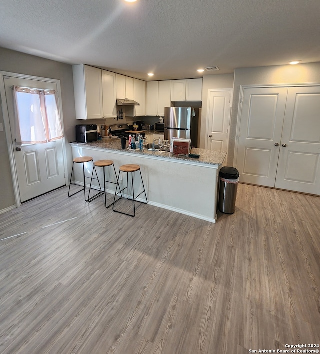 kitchen with stainless steel appliances, light hardwood / wood-style floors, kitchen peninsula, white cabinetry, and a textured ceiling