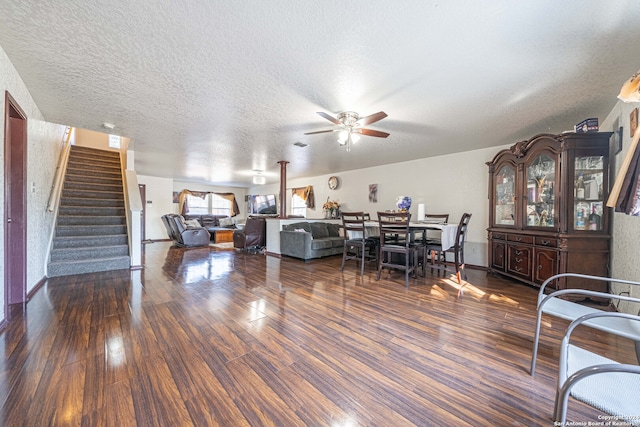 living room with a textured ceiling, ceiling fan, and dark wood-type flooring