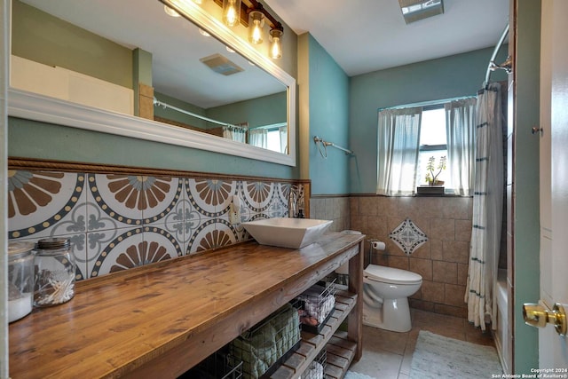 full bathroom featuring vanity, shower / bath combo with shower curtain, tile patterned floors, tile walls, and toilet