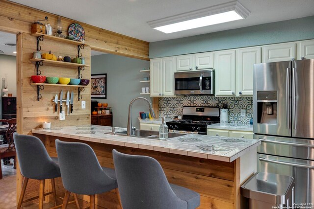 kitchen featuring stainless steel appliances, kitchen peninsula, white cabinets, and tile countertops