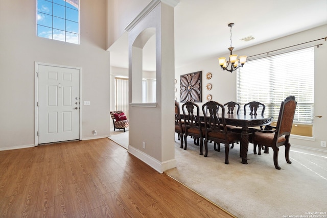 dining space with an inviting chandelier, hardwood / wood-style floors, a towering ceiling, and a healthy amount of sunlight