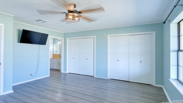 unfurnished bedroom featuring ceiling fan, hardwood / wood-style flooring, multiple windows, and ensuite bath