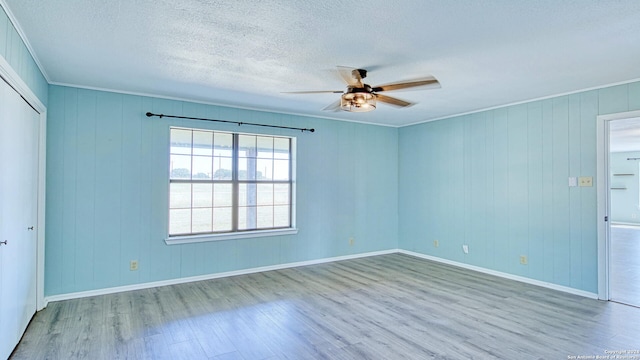 spare room with wooden walls, ceiling fan, wood-type flooring, ornamental molding, and a textured ceiling