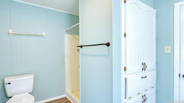 bathroom featuring wood-type flooring, wood walls, toilet, a shower, and a textured ceiling