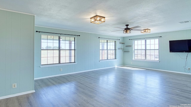 empty room with wooden walls, ceiling fan, hardwood / wood-style floors, and a textured ceiling