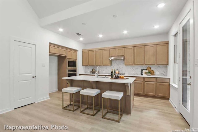 kitchen with sink, a kitchen island with sink, a kitchen bar, built in microwave, and light wood-type flooring