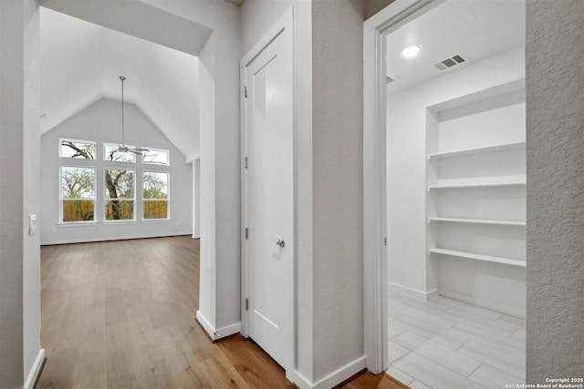 corridor with built in shelves, lofted ceiling, and light wood-type flooring