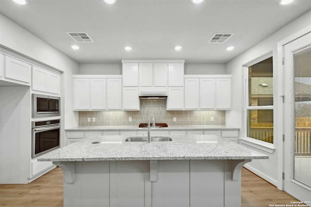 kitchen with white cabinetry, a kitchen bar, a kitchen island with sink, stainless steel appliances, and light stone countertops