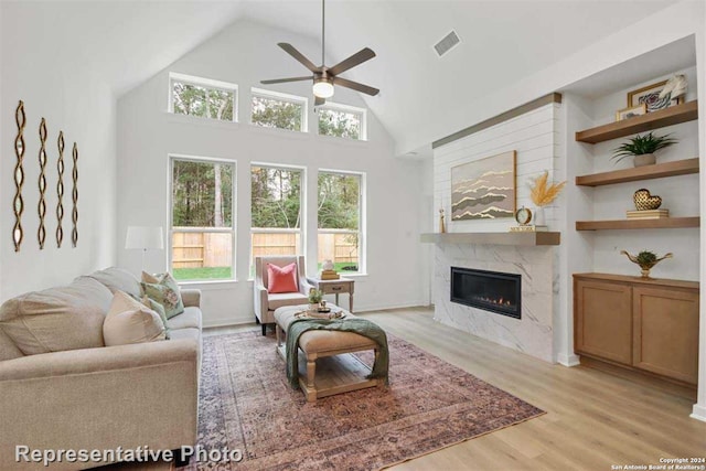 living room featuring light hardwood / wood-style floors, ceiling fan, a fireplace, a towering ceiling, and built in shelves